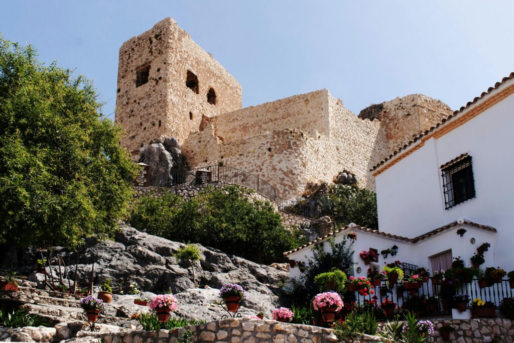 Stunning view of an ancient castle in Luque, Spain, surrounded by vibrant flowers and rocky landscape.