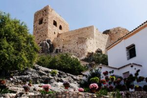 Stunning view of an ancient castle in Luque, Spain, surrounded by vibrant flowers and rocky landscape.