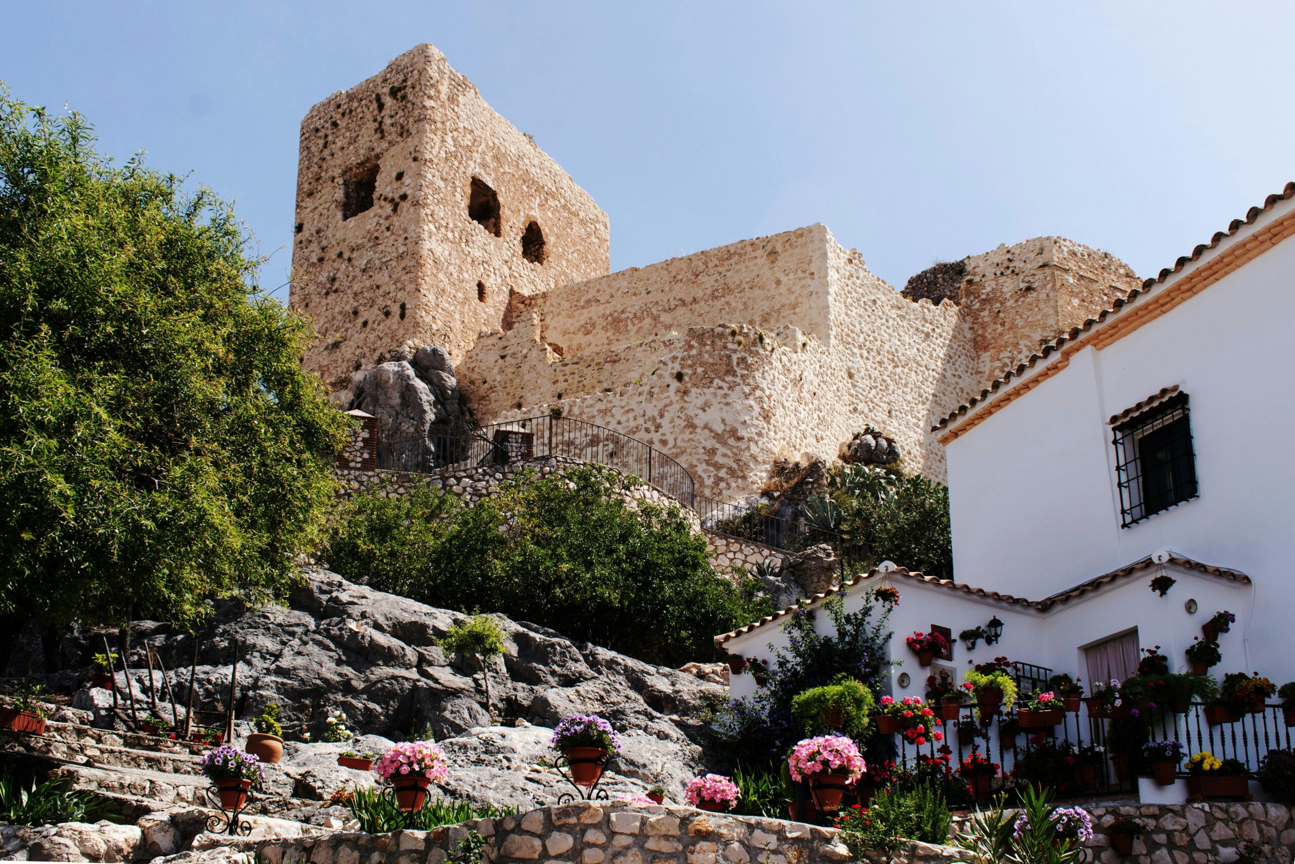 Stunning view of an ancient castle in Luque, Spain, surrounded by vibrant flowers and rocky landscape.